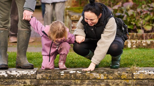 Adult and child bent down looking into a pond